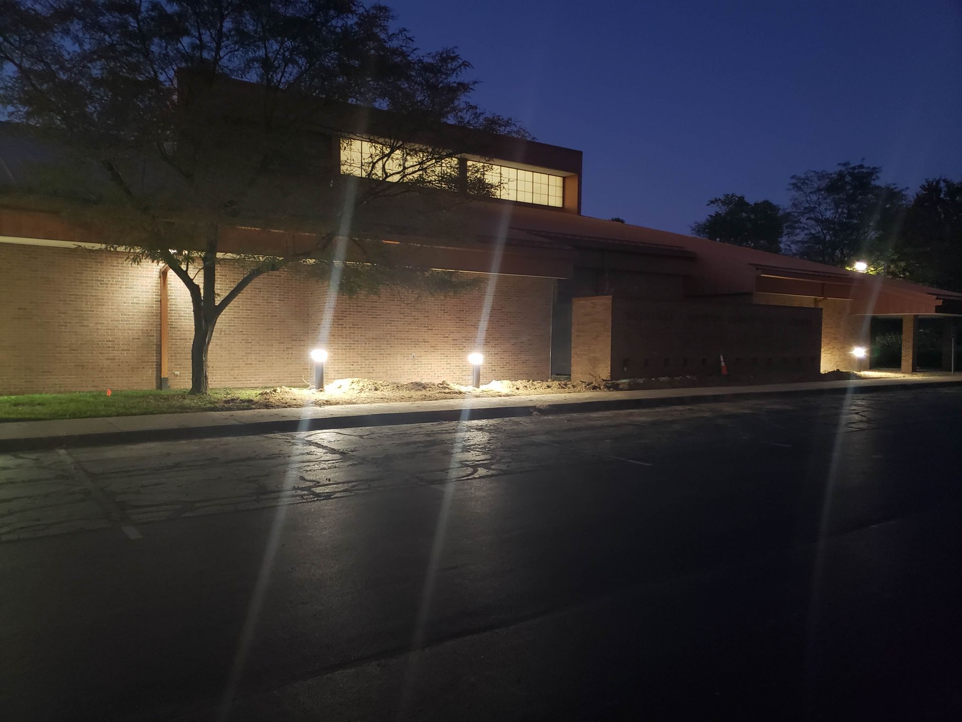 Exterior of a brick building at dusk, lit by ground lamps and building lights.