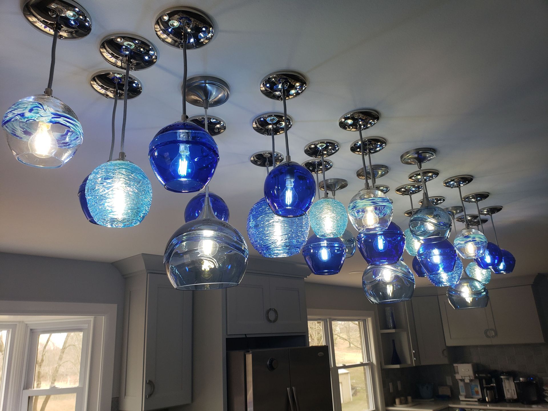 Ceiling lights: Multiple blue and silver globe pendant lights in a kitchen, above cabinets and windows.