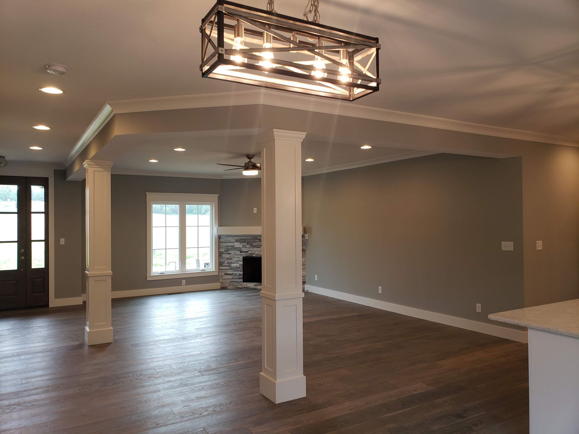 Open-concept living room with white pillars, hardwood floors, fireplace, and modern light fixture.