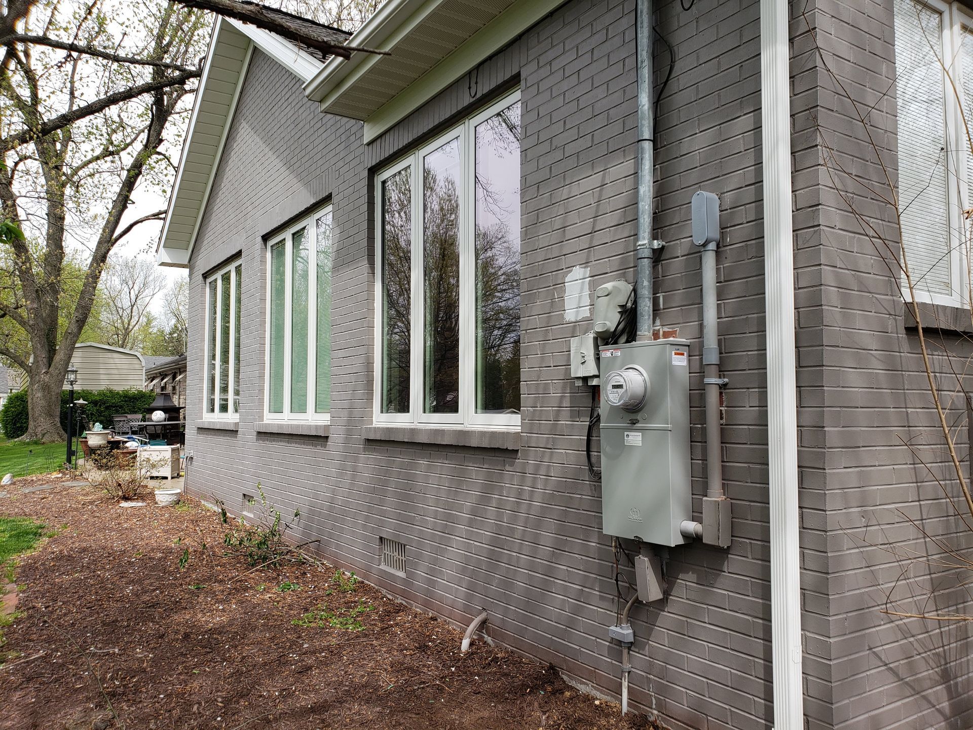 Gray brick house exterior with windows, electrical meter, and conduit.