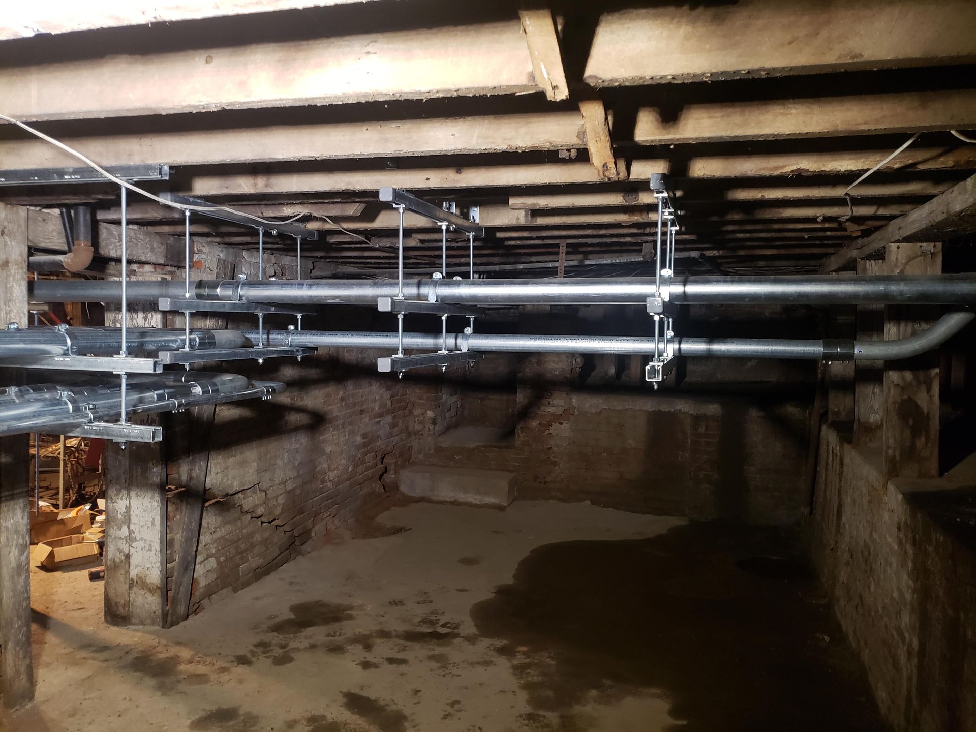 Underground space with pipes and wooden beams. Water on the floor.