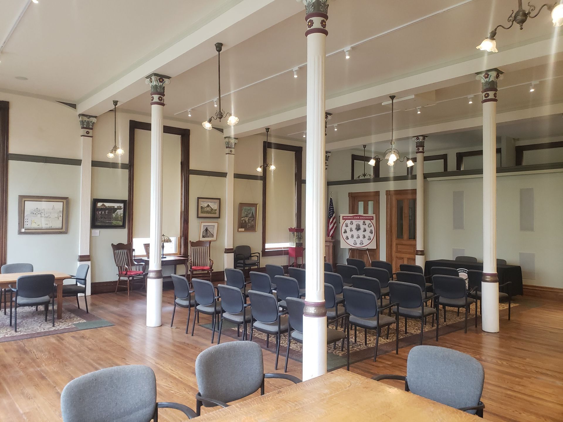 Interior of a room with rows of chairs, tables, white columns, and artwork on the walls.