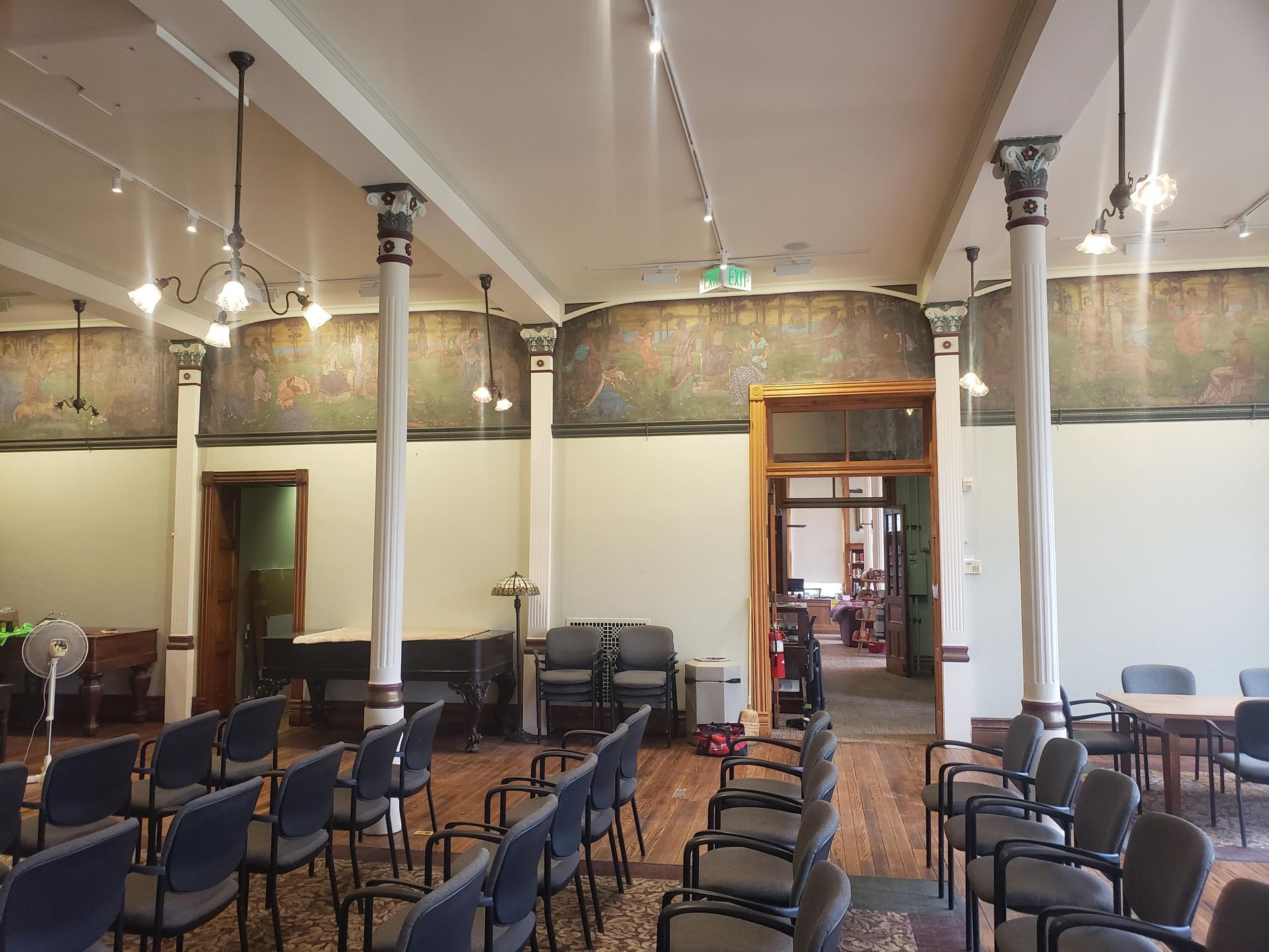 An empty meeting room with rows of chairs, columns, and a doorway leading to another room.