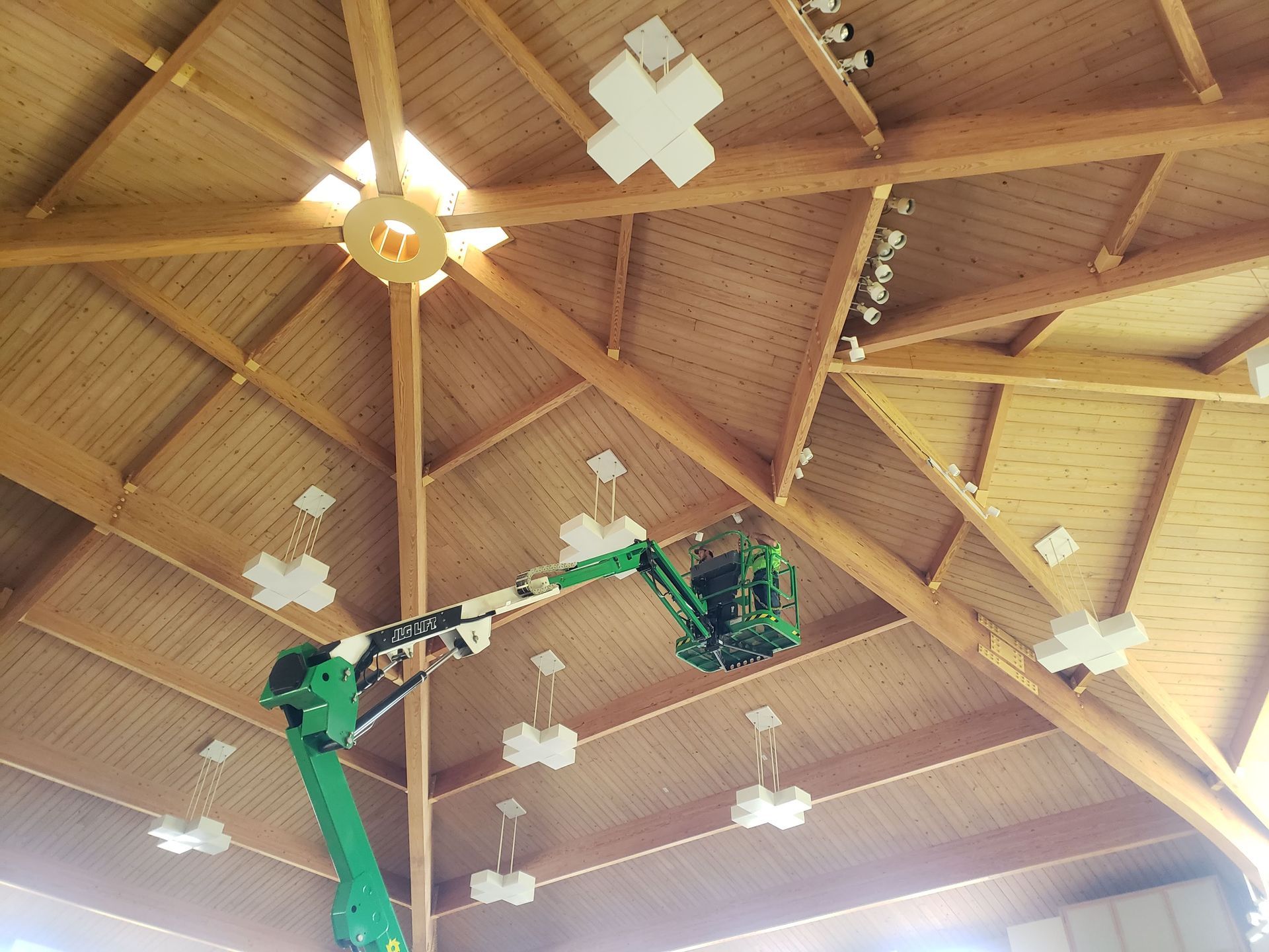 Green lift truck near a wooden cathedral ceiling with installed white fixtures.