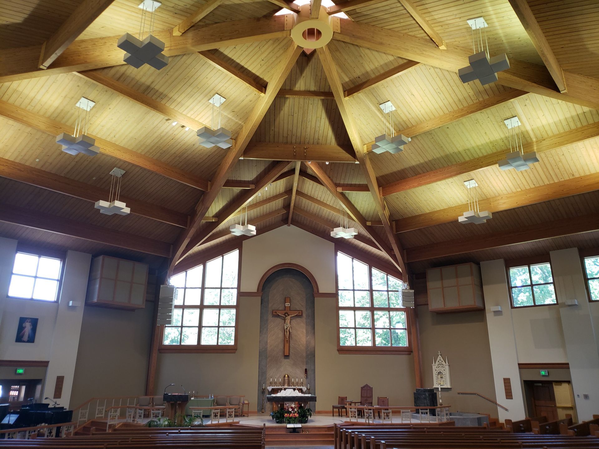 Interior of a church with wooden ceiling and cross, altar centered with stained glass windows.