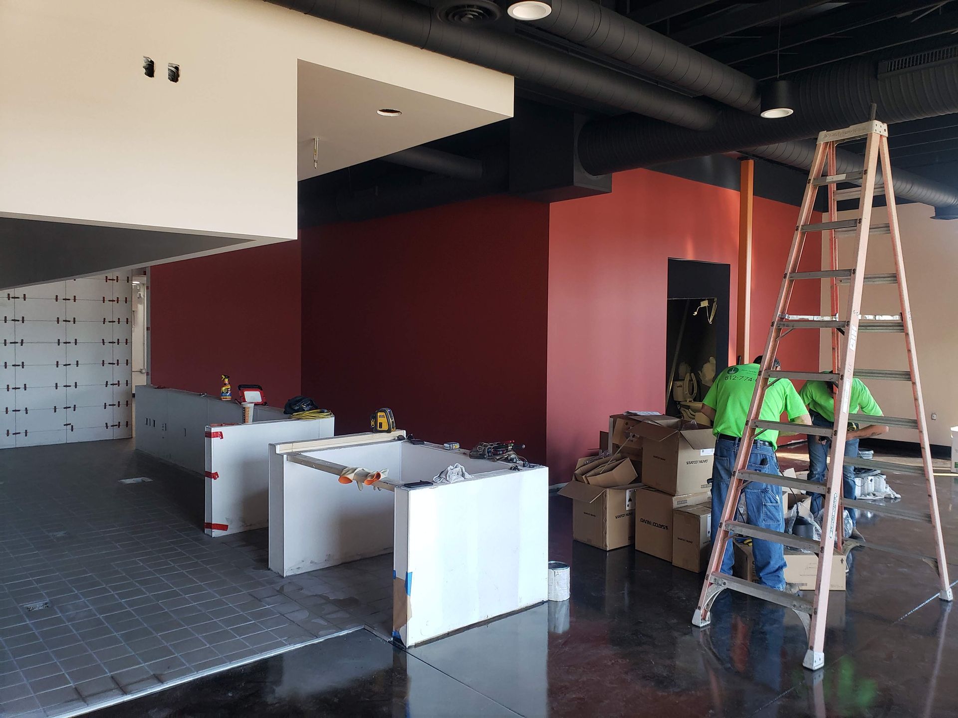 Interior under construction with red walls, workers, and a ladder.