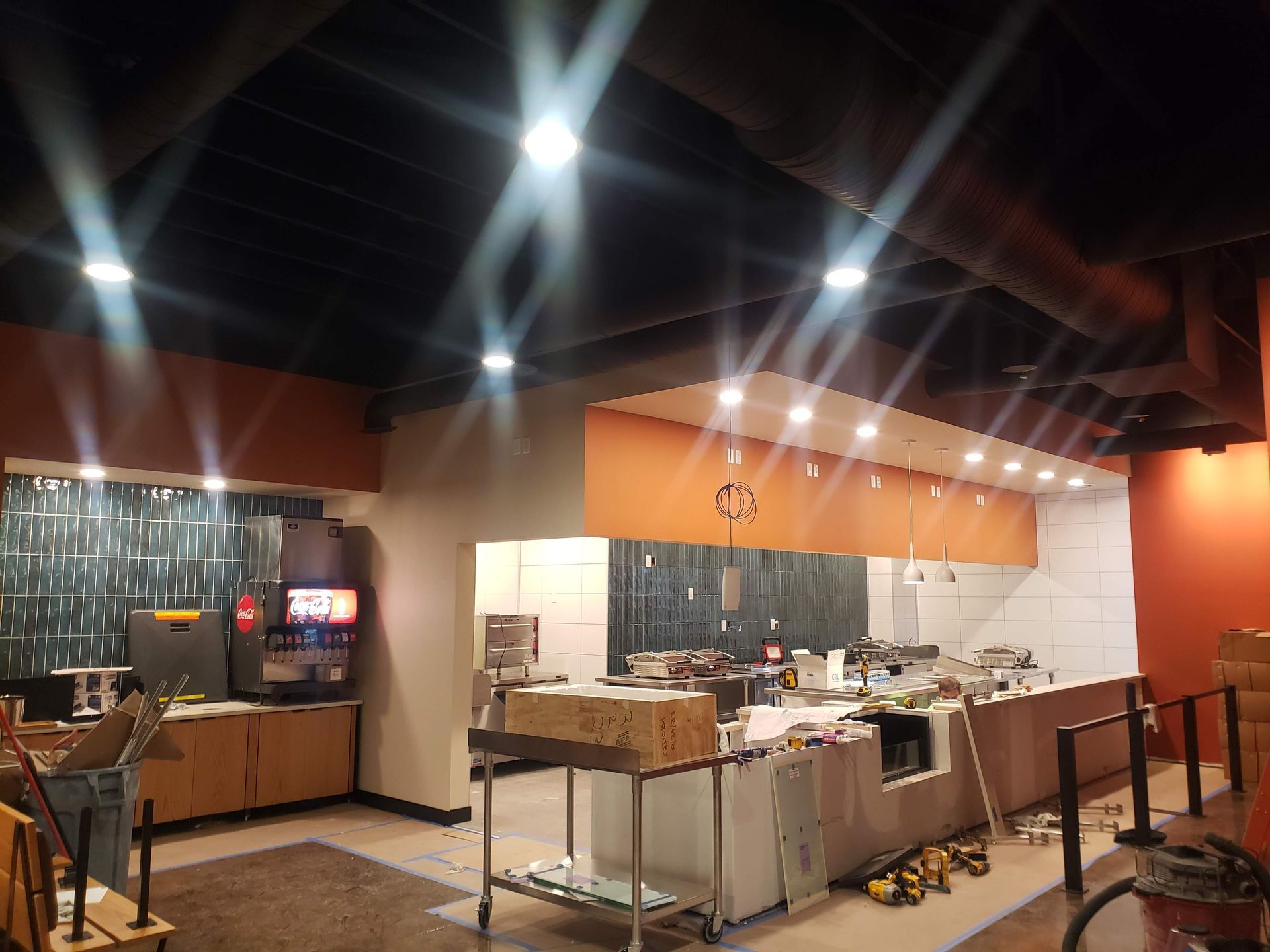 Interior of a restaurant under construction with exposed ductwork, orange accents, and bright overhead lights.