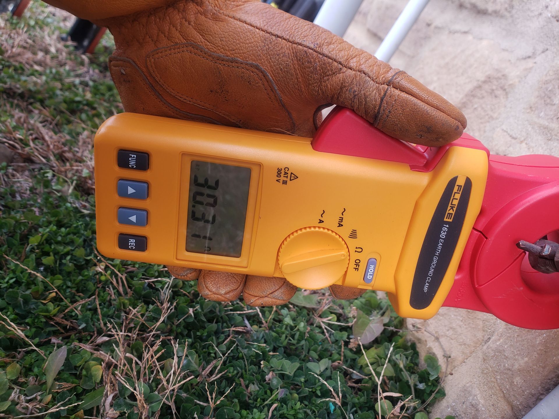 Person wearing a brown glove holds a yellow multimeter, reading 30.3.