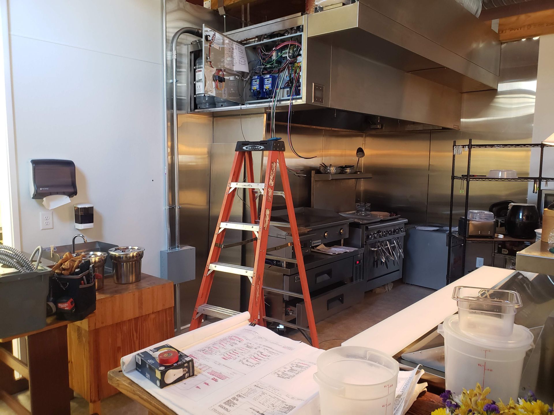 Kitchen with ladder set up, electrical panel open above the stove, and work in progress.