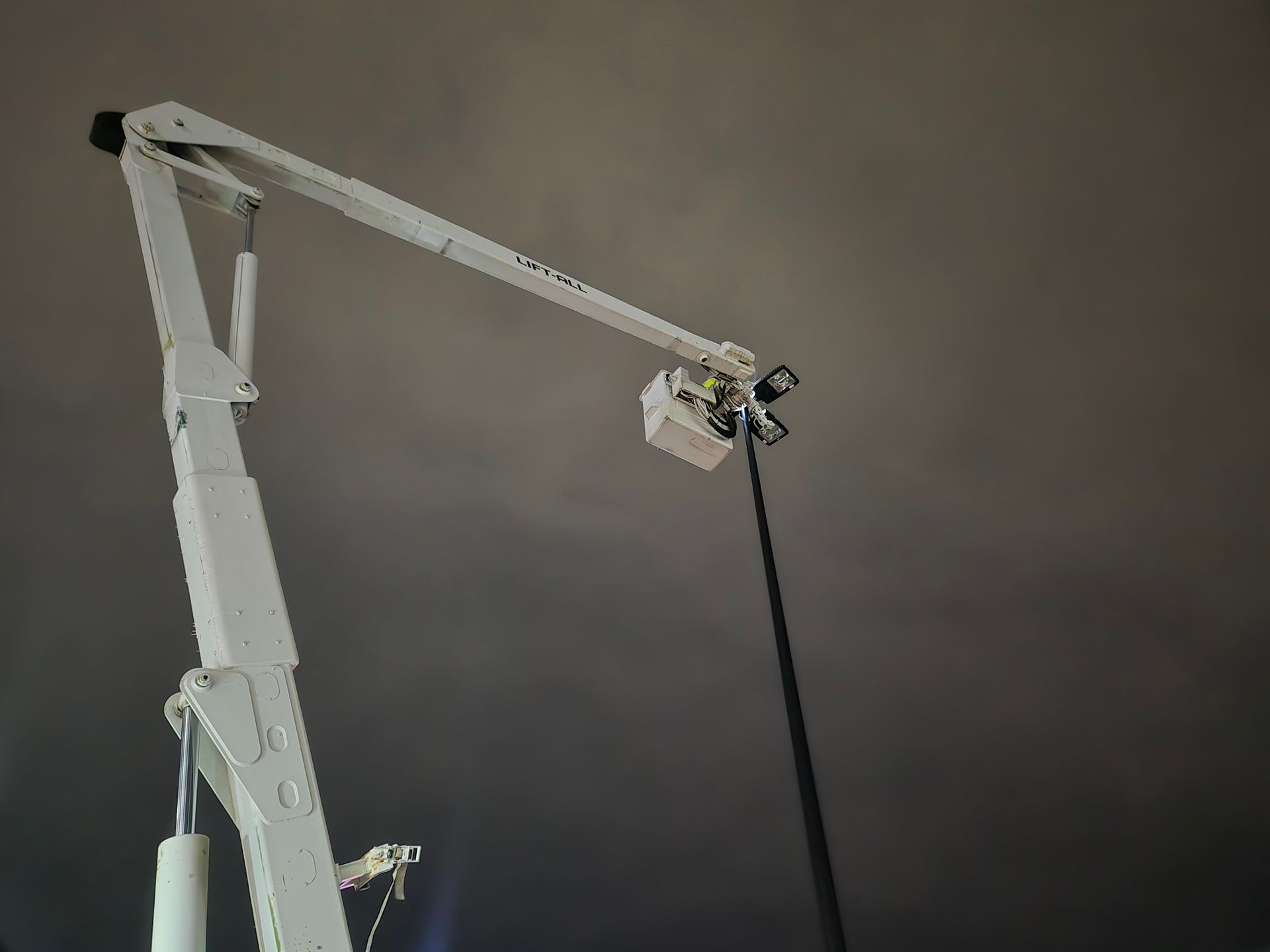 White aerial lift with a light fixture extended against a dark sky.