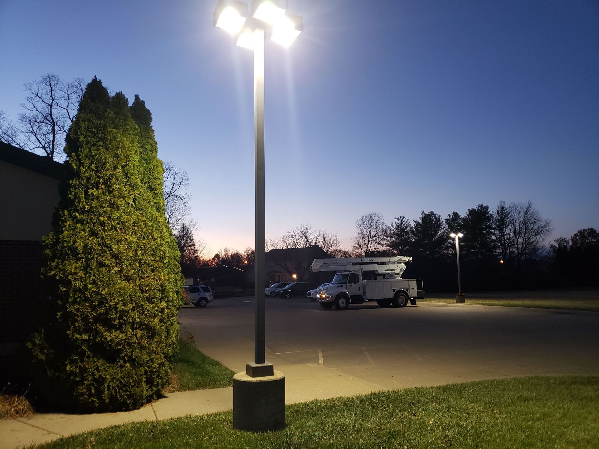Parking lot at dusk, lit by tall lamps; a work truck is parked near the center.