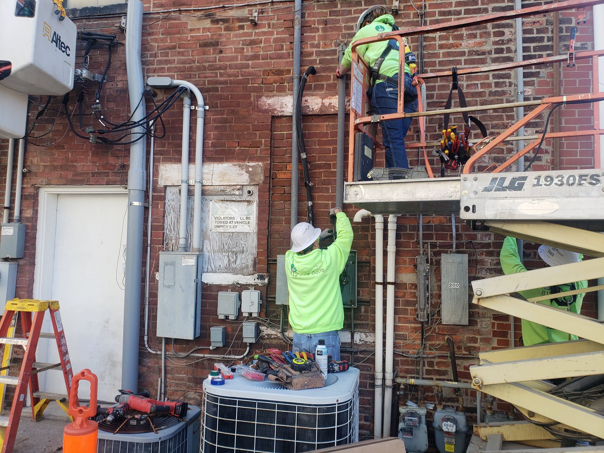 Two utility workers on a lift installing electrical wiring on a brick building.