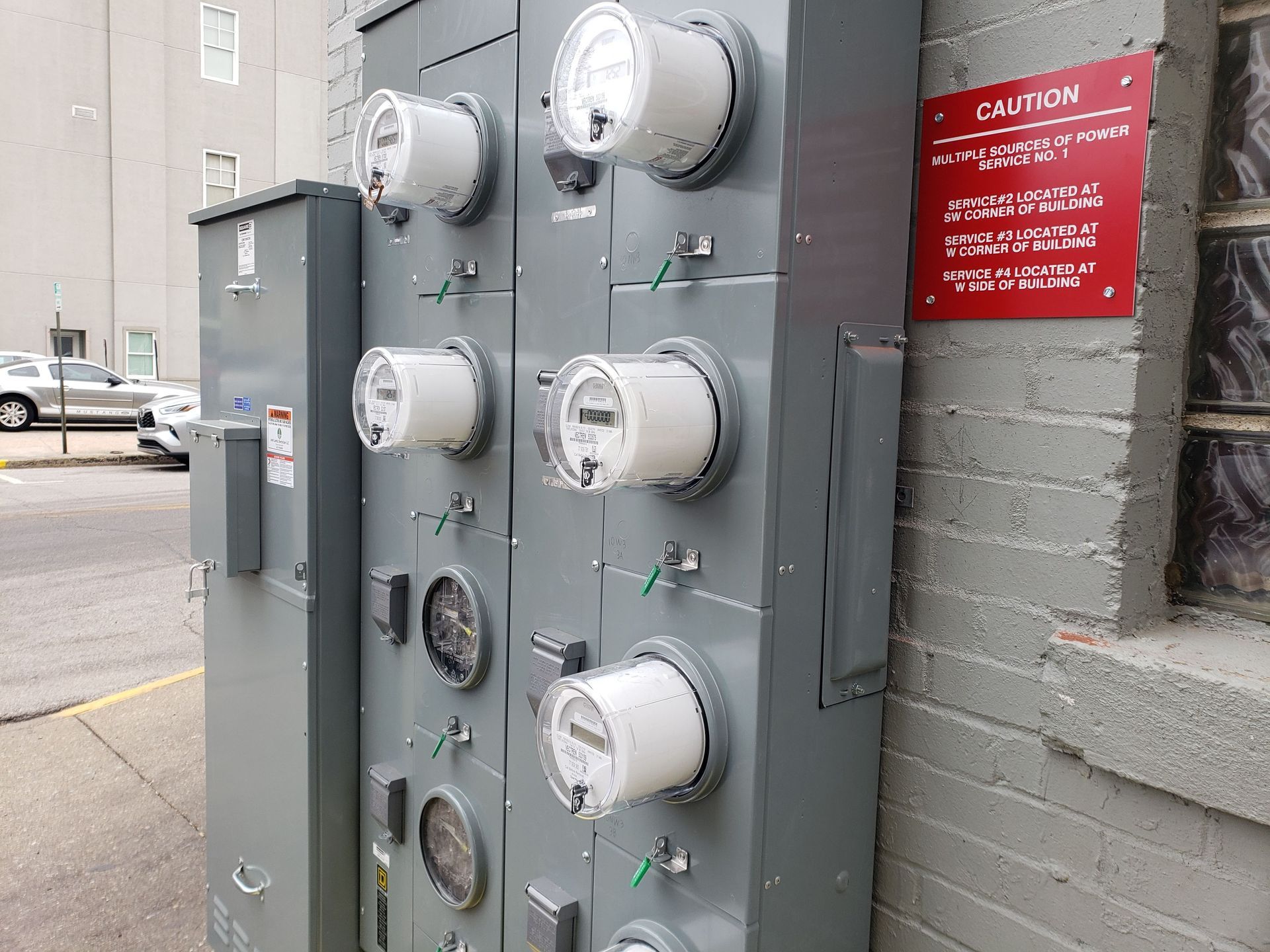 Gray electrical meters on an exterior wall with a red caution sign.