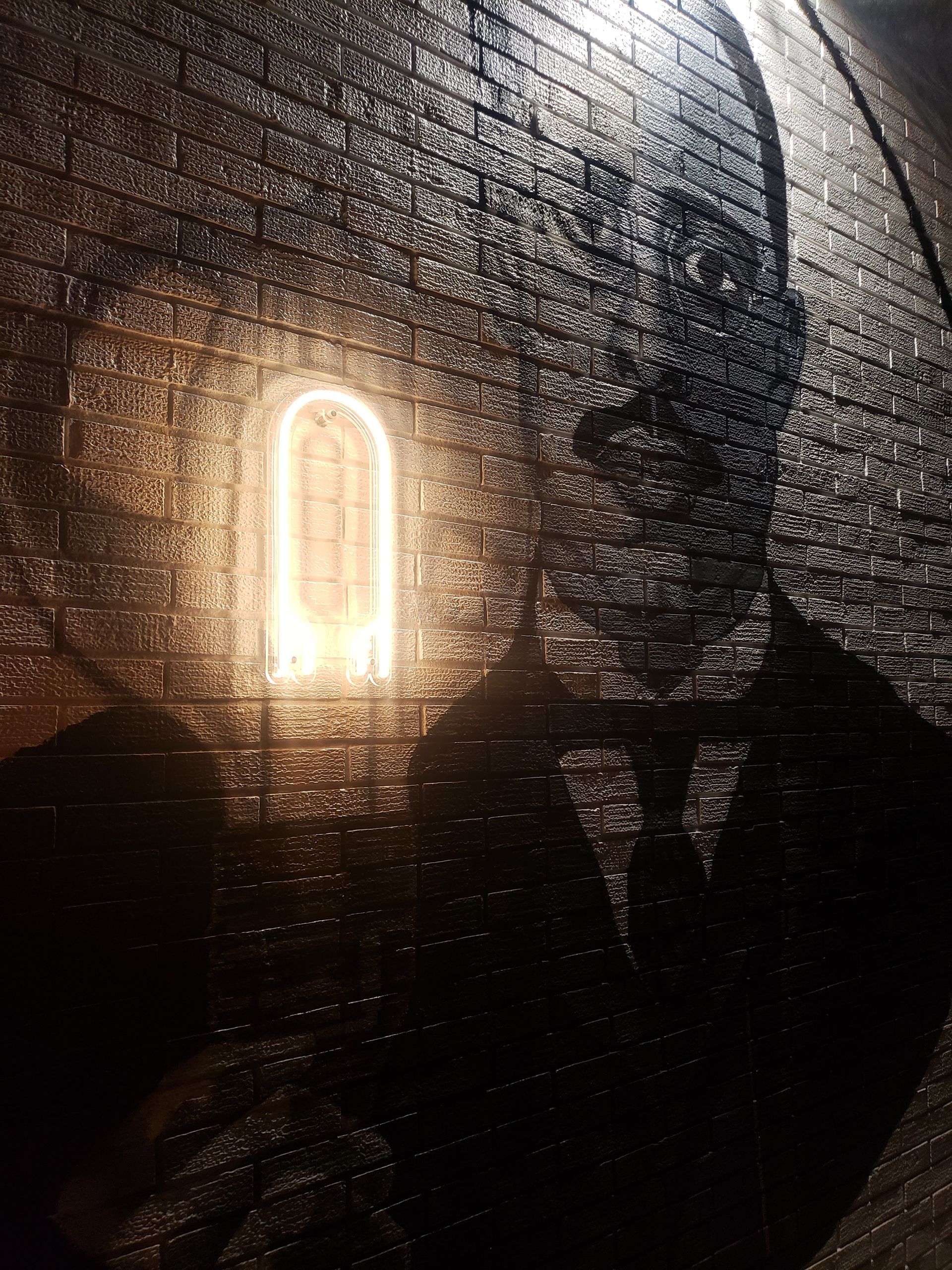 Glowing archway in a brick wall, casting a bright light. Large silhouette of a person on the right.
