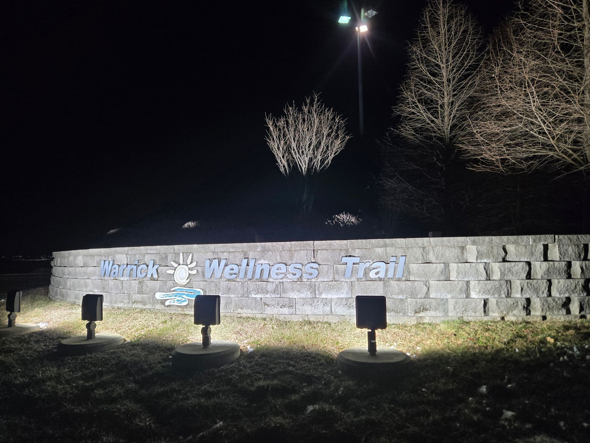 Sign for the Murdock Wellness Trail at night, illuminated by ground lights.