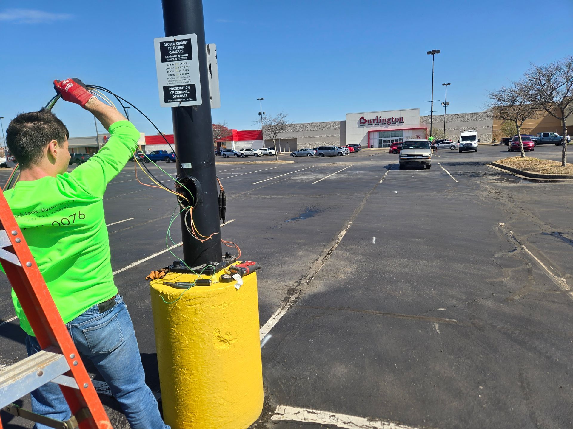 A person in a neon green shirt works on a utility pole in a parking lot.