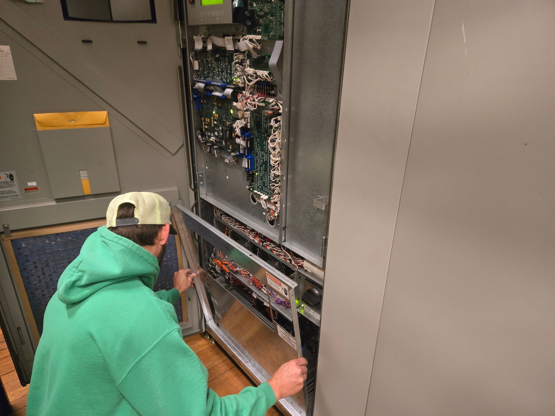 Person in green hoodie opening a metal cabinet containing circuit boards.