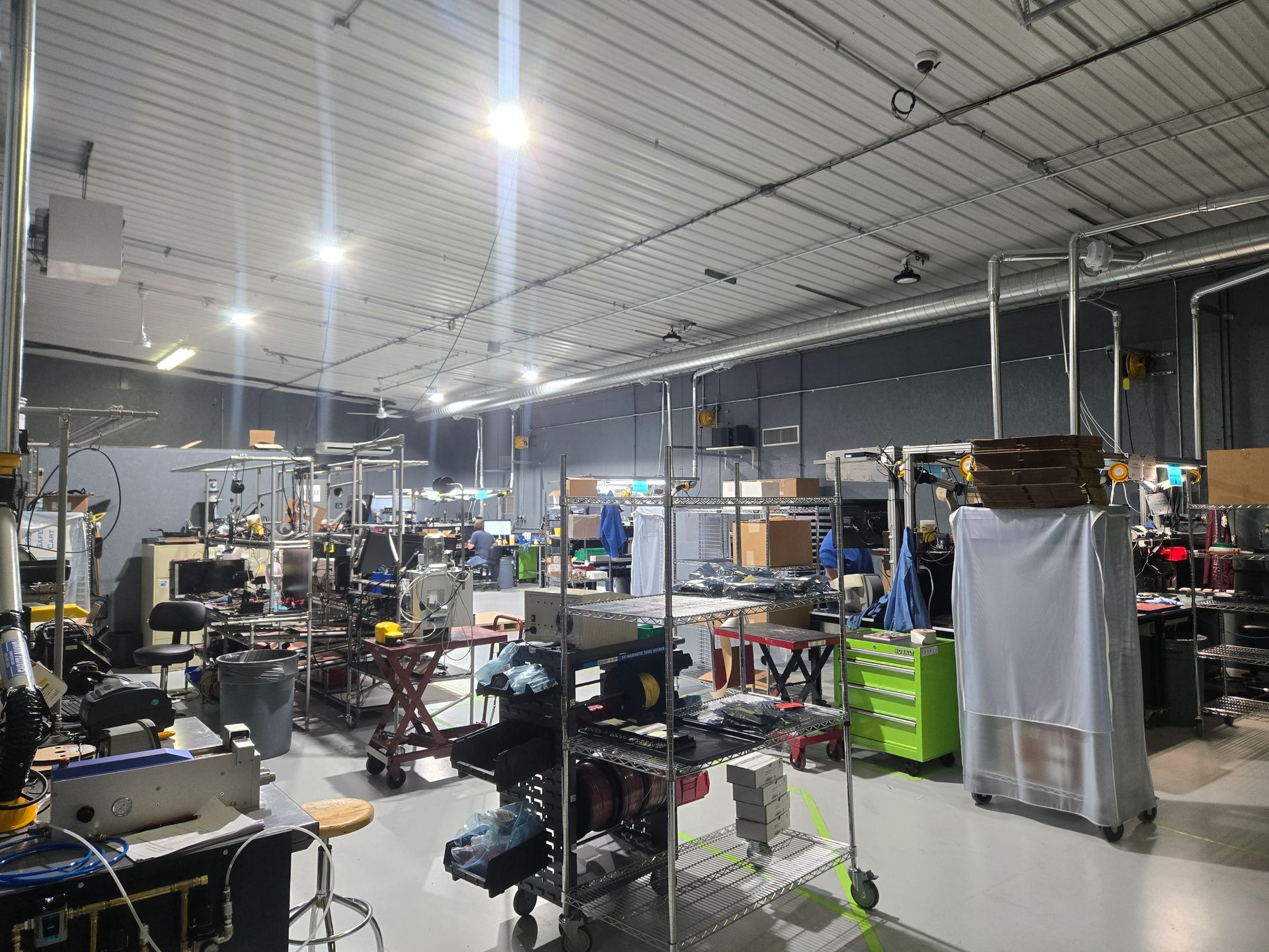 Workshop interior with various tools and equipment; people working in the background. Bright lighting.