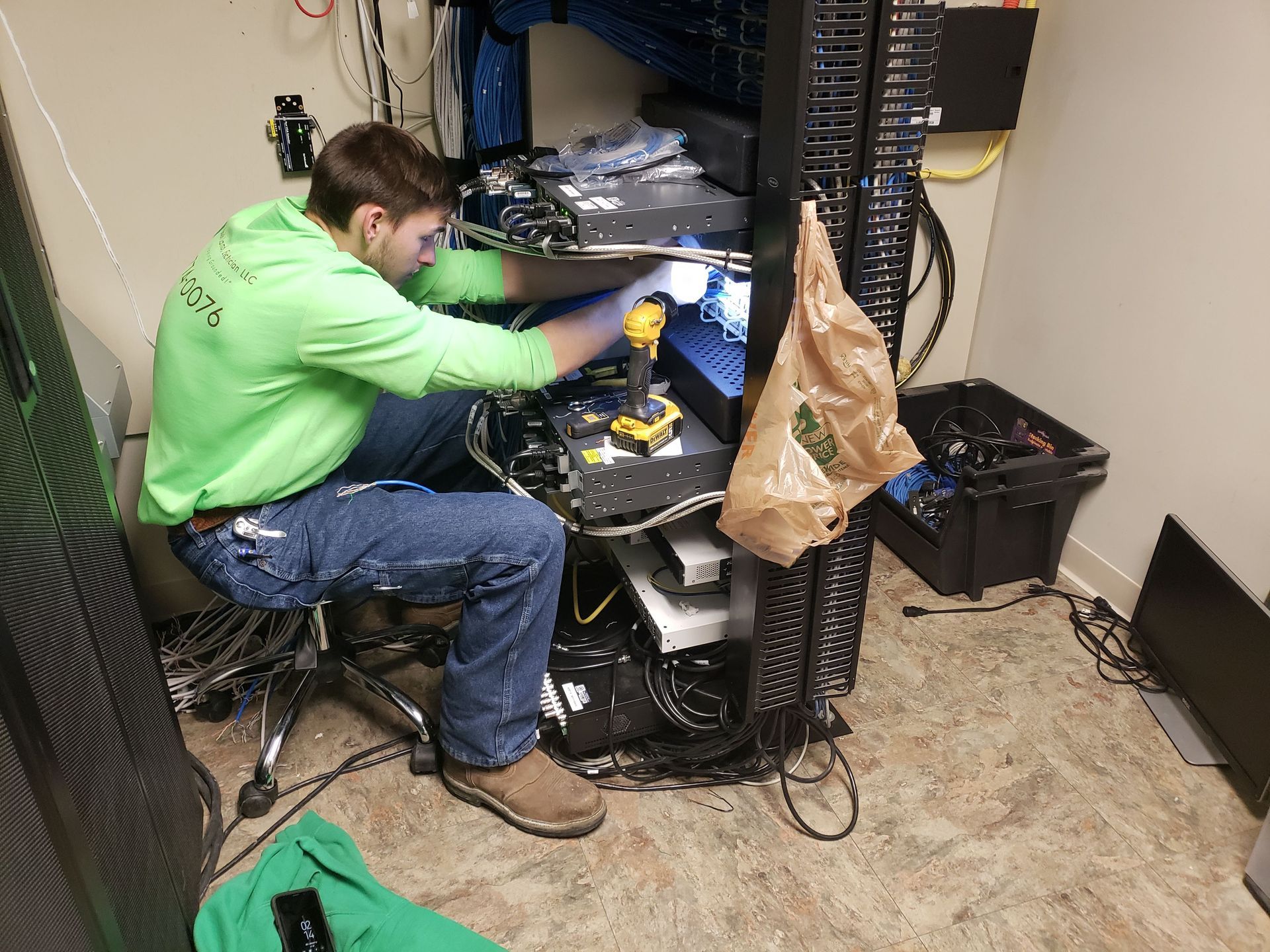 Man in green shirt working on server rack in small room.