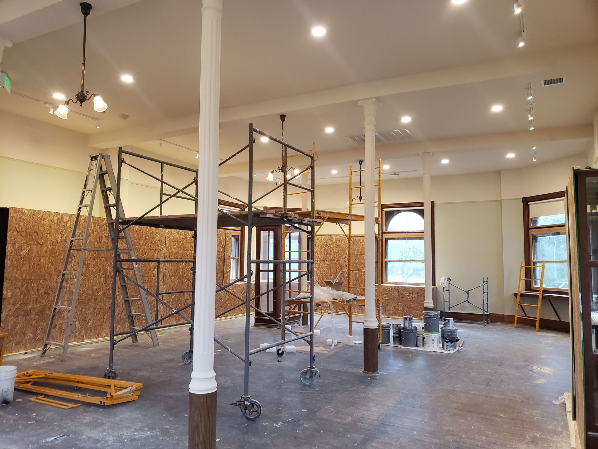 Interior room under renovation with scaffolding, columns, and plywood walls.
