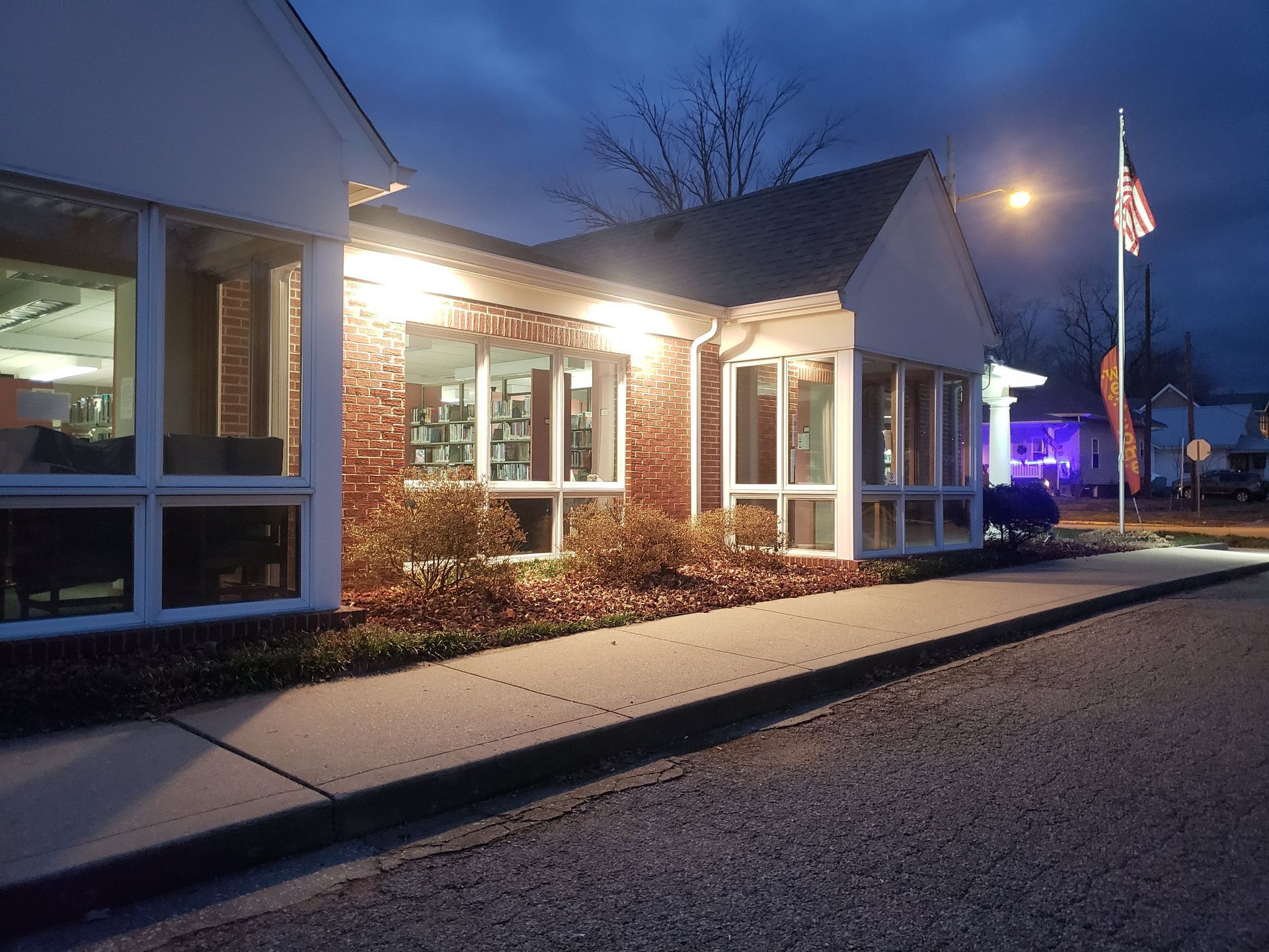 Building with brick facade and large windows illuminated at dusk, American flag in view.