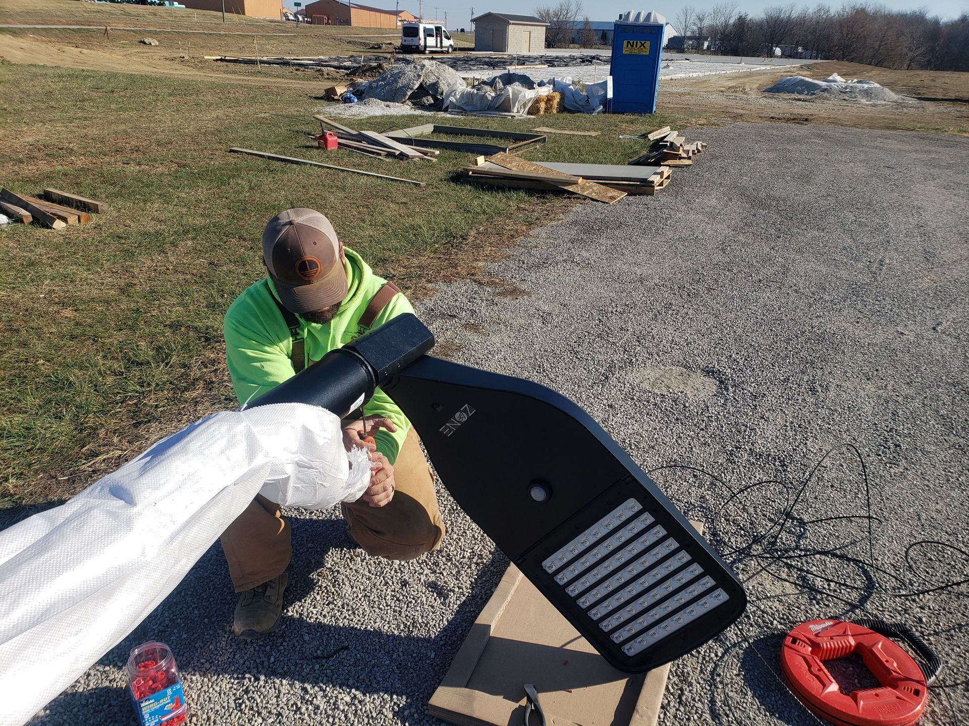 Person installing a black street light on a gravel surface outdoors.