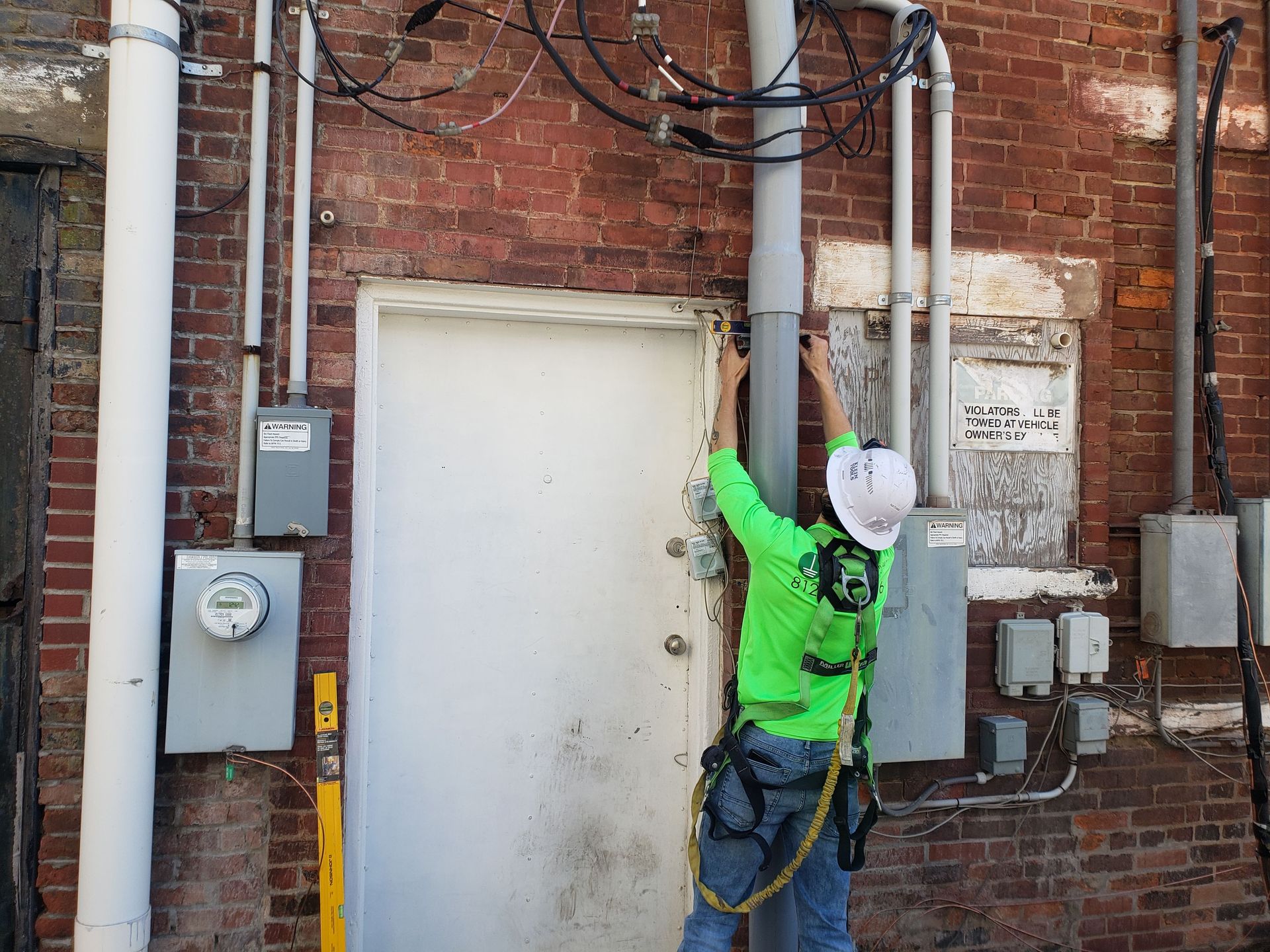 Person in safety gear working on wires near a door and brick wall.