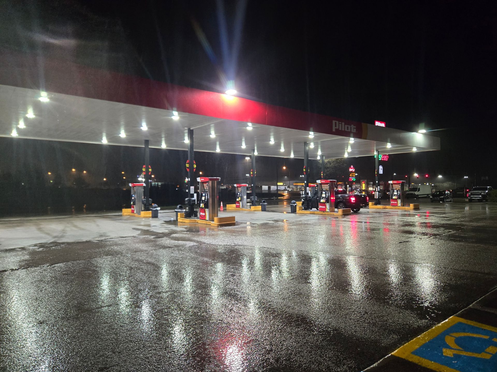 Gas station at night with wet pavement reflecting bright lights from the canopy and pumps.