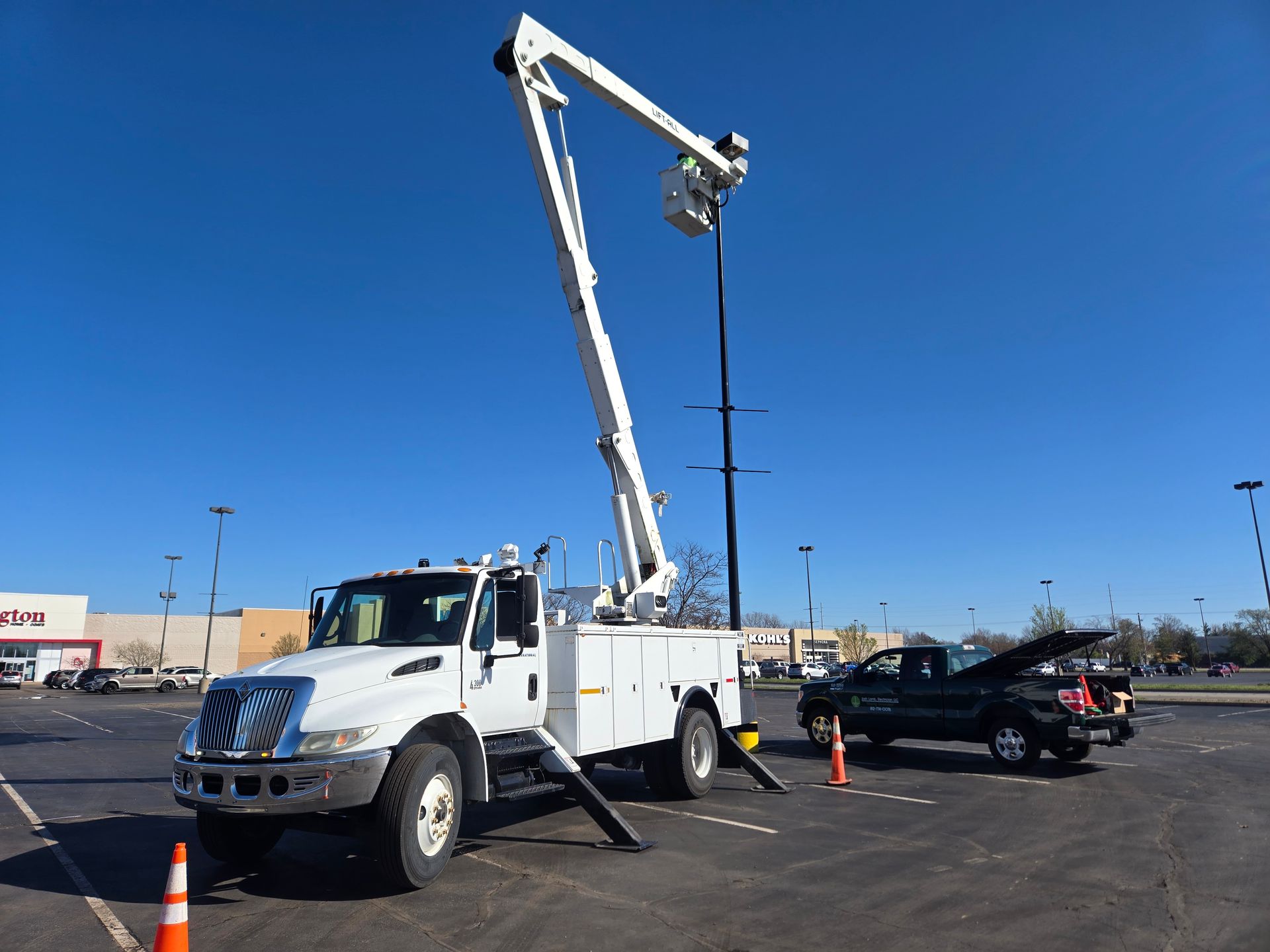 White utility truck with extended boom, working on a power line in a parking lot.