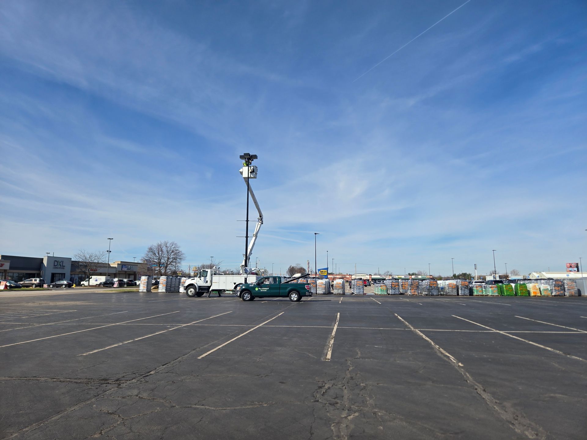 A utility truck with an extended boom in a nearly empty parking lot under a blue sky.