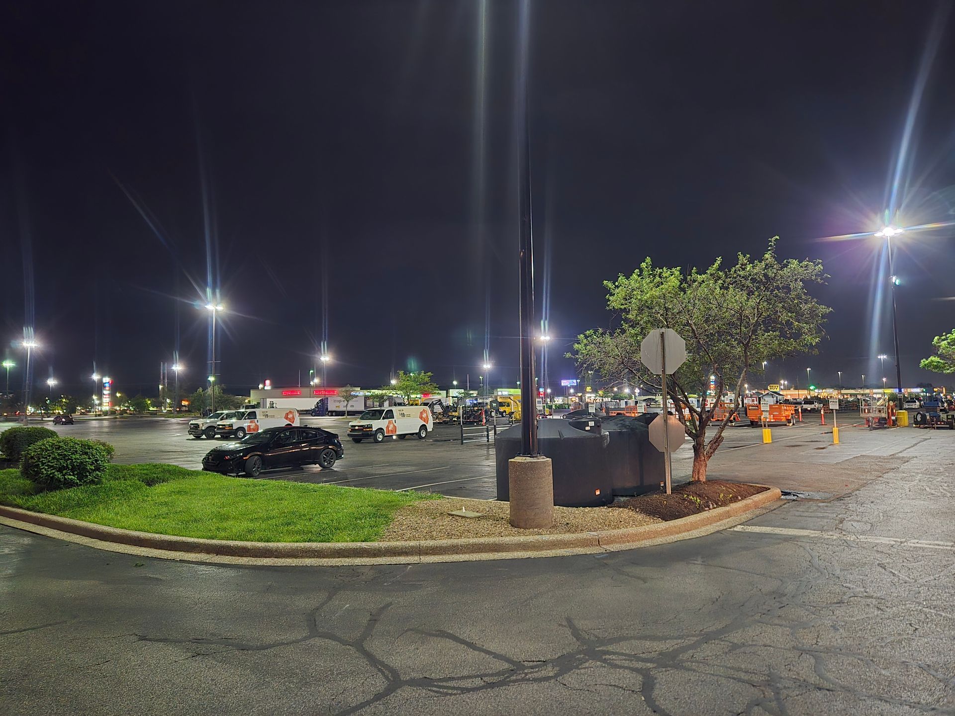 Nighttime parking lot scene, cars parked near a building with bright overhead lights.