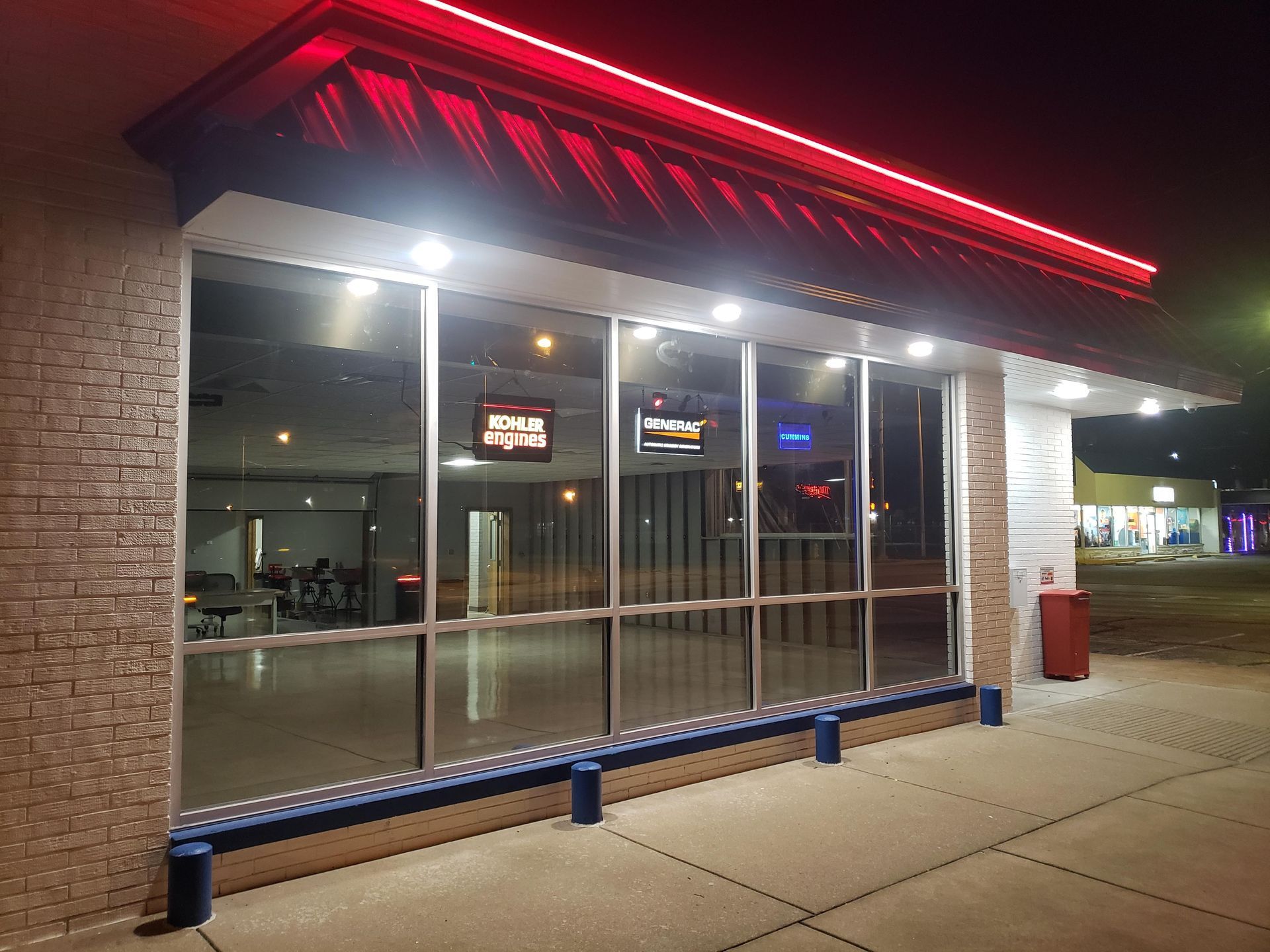 Exterior of a building with large windows, a red awning, and a blue bench. It is nighttime.