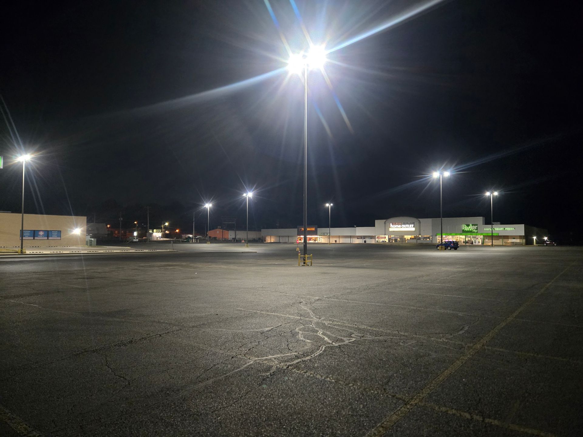 Empty, dark parking lot under bright streetlights at night; a person stands alone in the center.