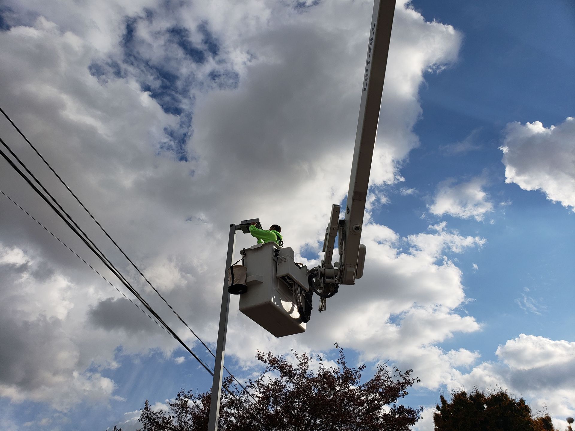Bucket truck near power lines against a cloudy sky. A worker in the bucket appears to be working.