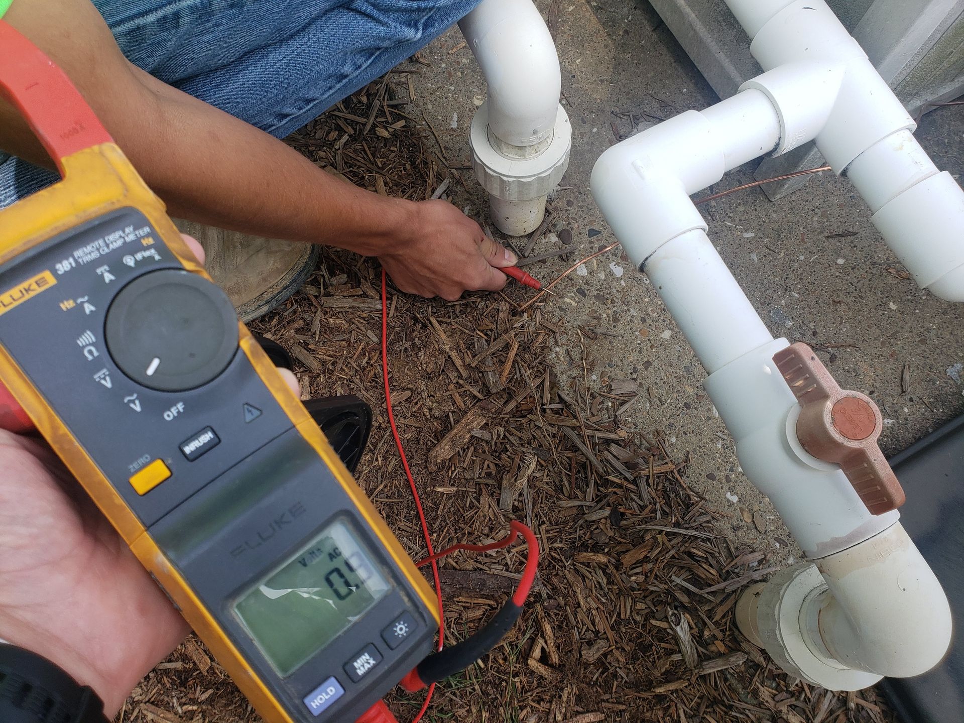 Person using a multimeter to test electrical current on pipes outdoors.