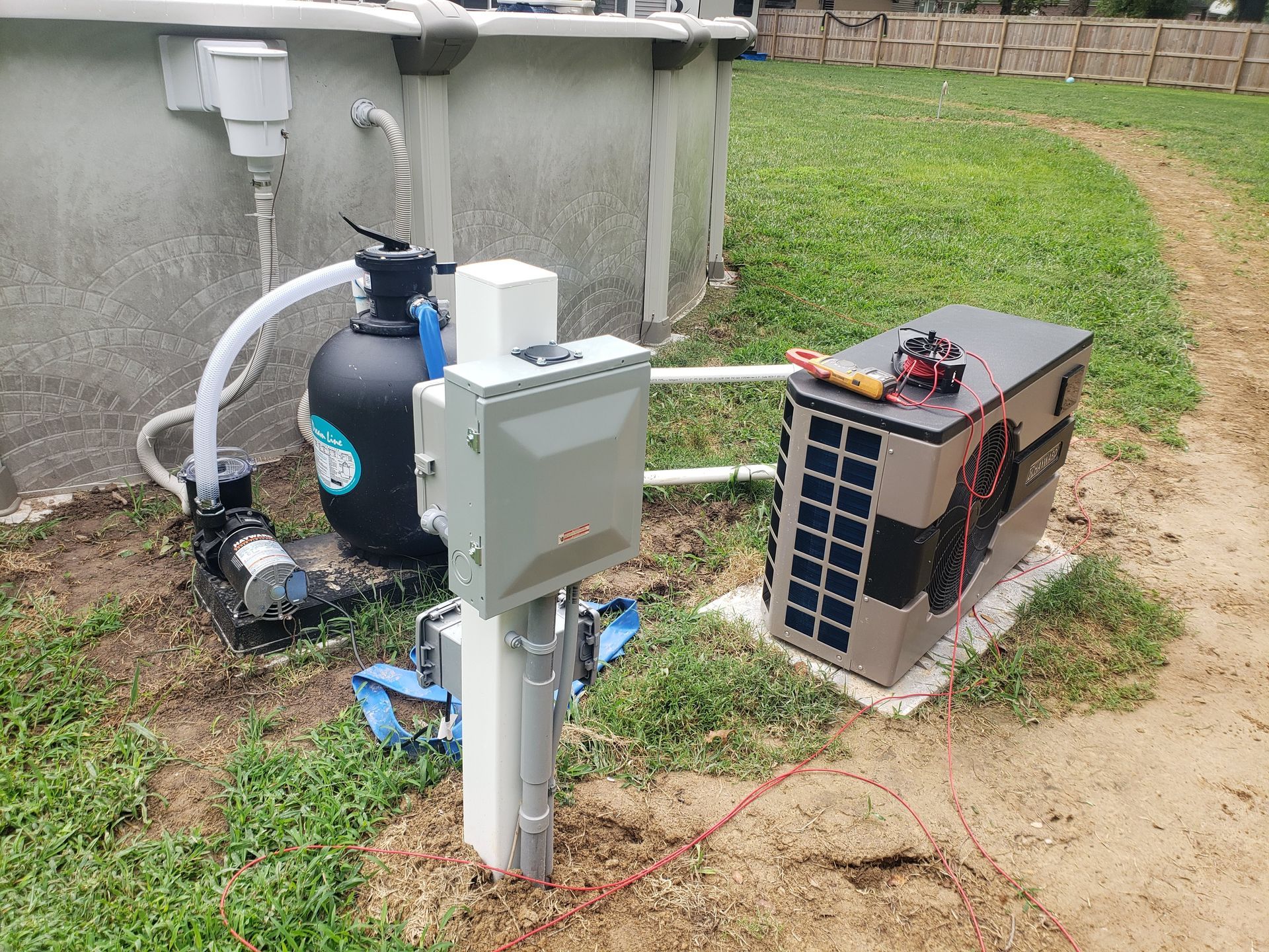 Pool equipment, including a filter, pump, electrical box, and heat pump, set up outdoors on grass.
