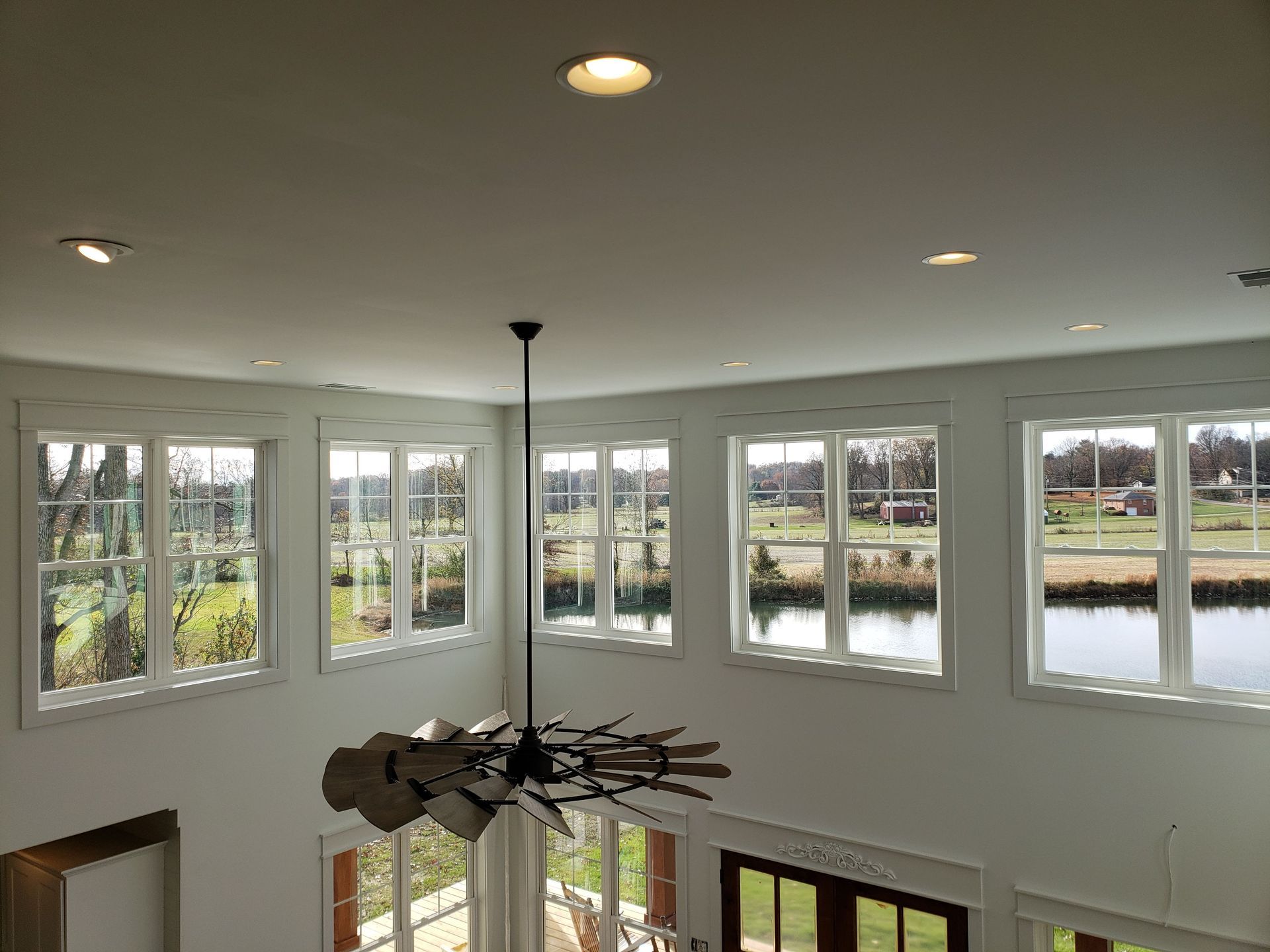 High-ceiling room with white walls, windows, and a black ceiling fan. Daylight streams in.