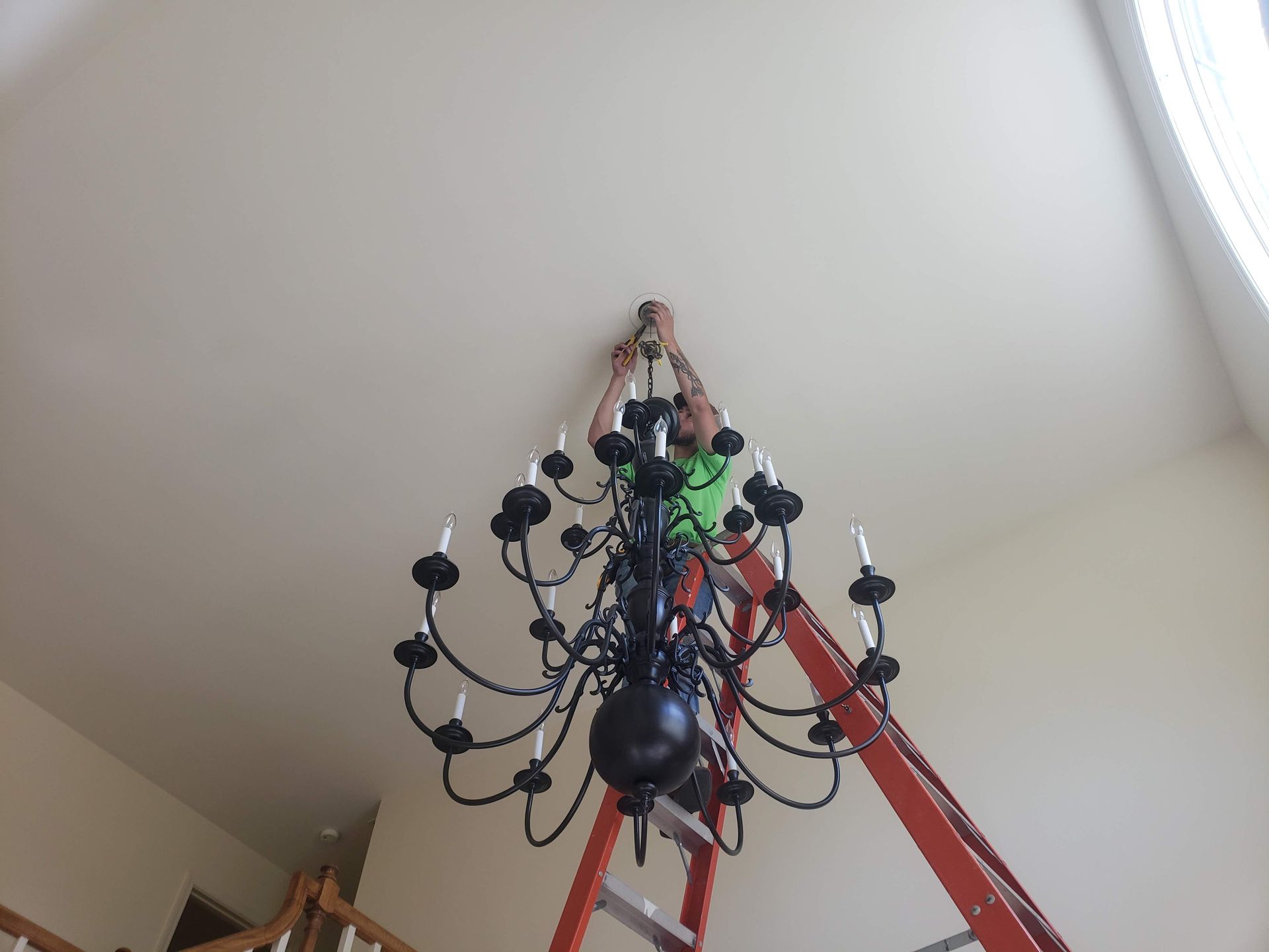 Person on ladder installing black chandelier on white ceiling.