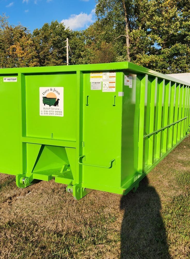 Green dumpster outdoors on a grassy area, logo visible.