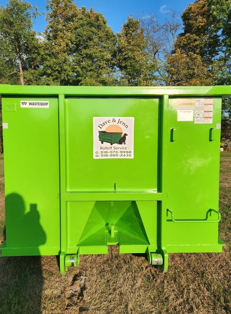Green dumpster with company logo in front of trees and a blue sky.