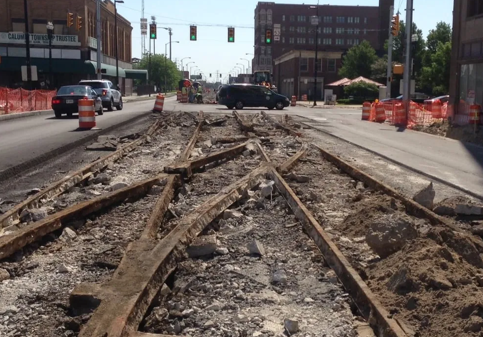 Road construction with exposed old train tracks; orange barriers line the street.