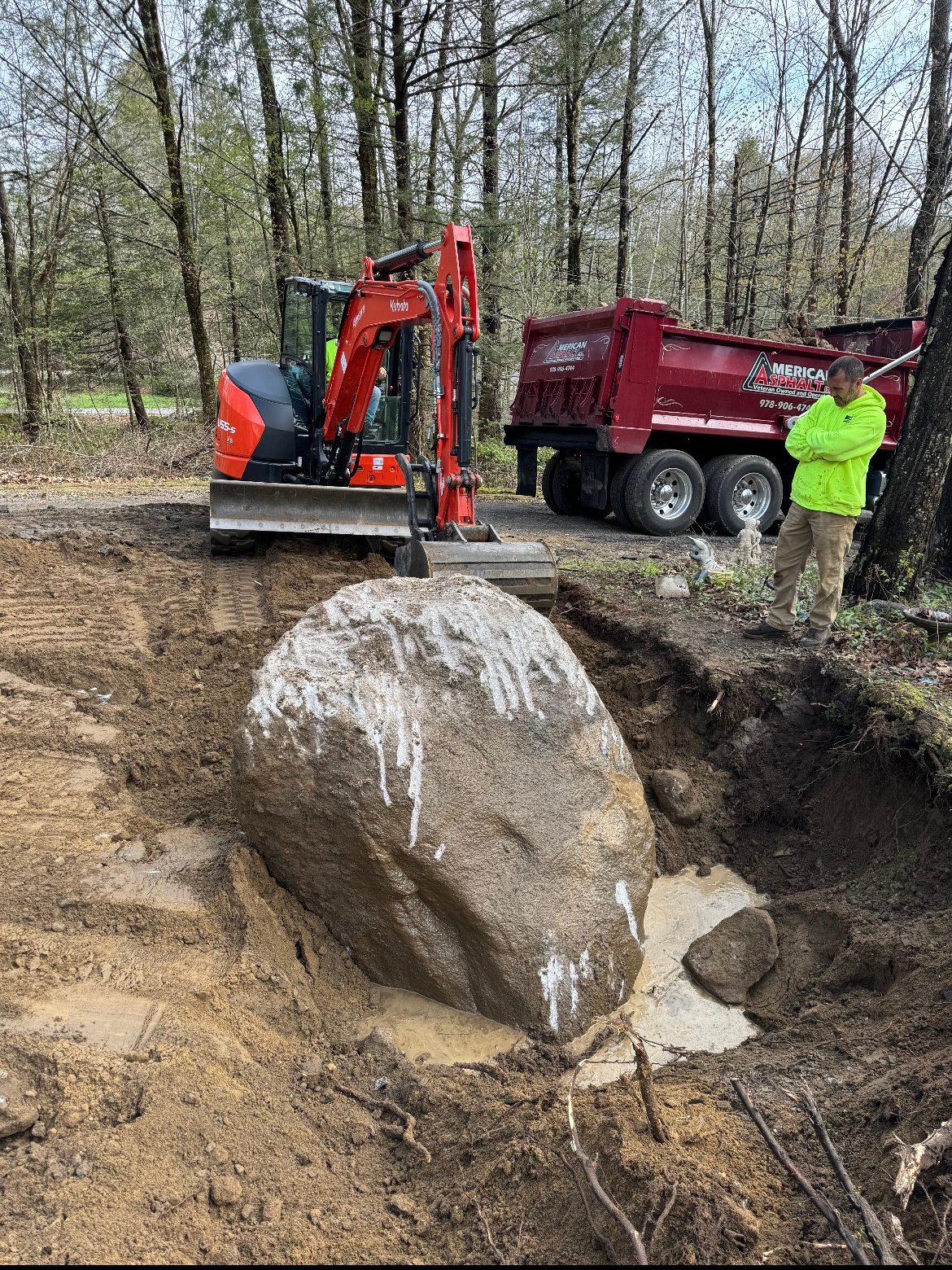 A man is standing next to a large rock next to a dump truck.
