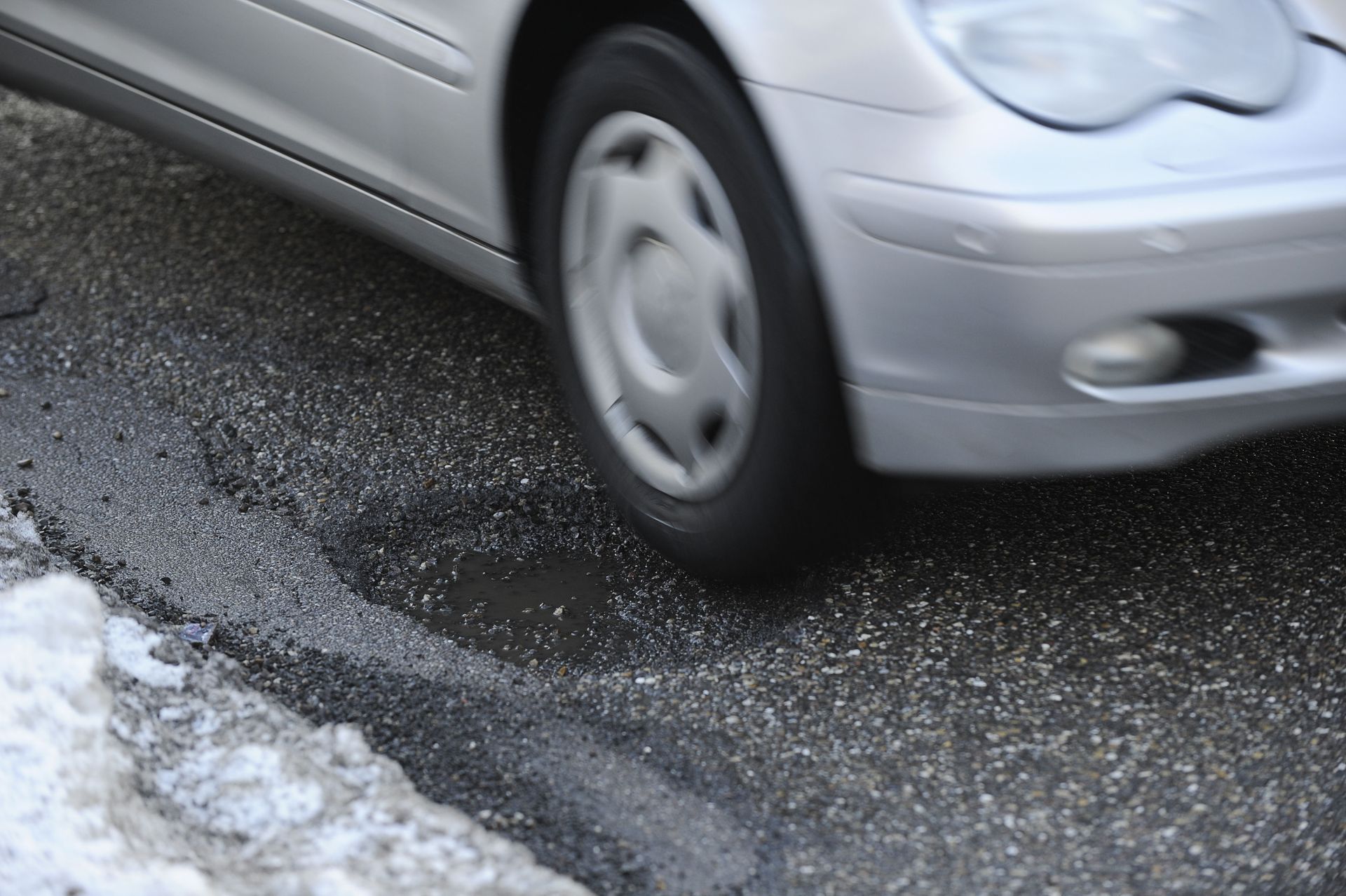 Silver car driving on wet road with snow on the side.