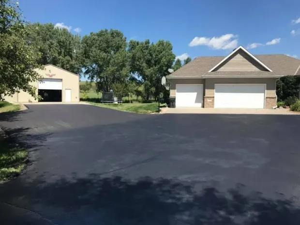 Paved driveway leading to a two-car garage and detached outbuilding on a sunny day.