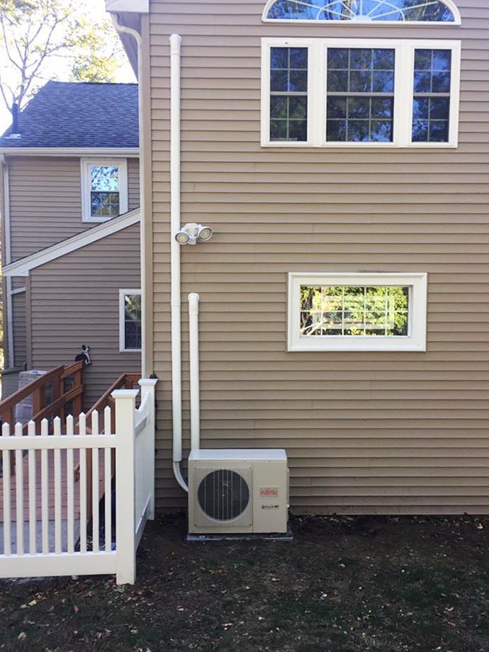 A house with a white picket fence and a white air conditioner on the side of it.