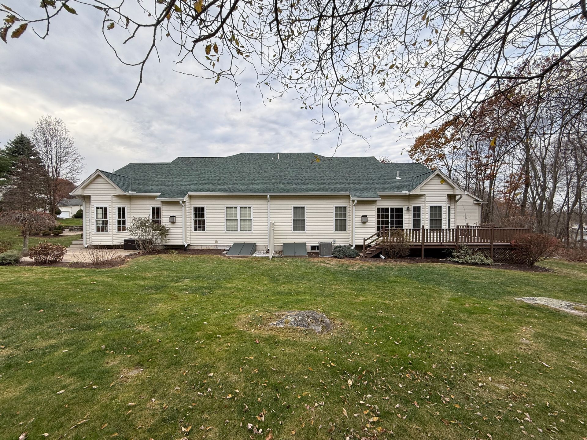 Single-story beige house with a green roof and front porch, set behind a wide grassy lawn