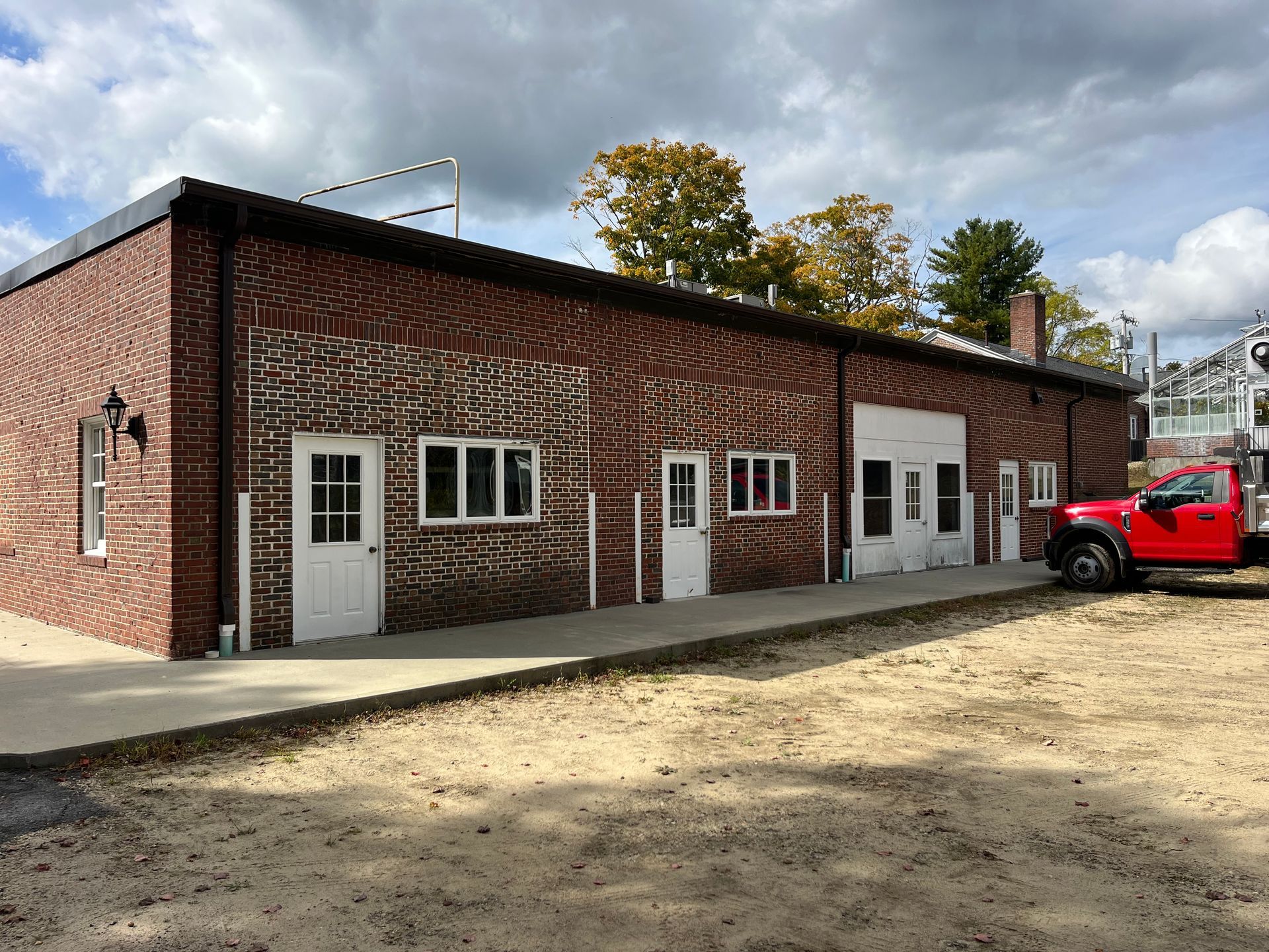 Brick building with multiple white doors and windows, a red truck parked beside it, and a dirt lot in front