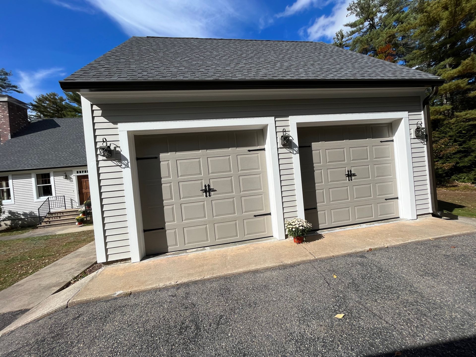 Two-car garage with beige doors and light siding under a partly cloudy blue sky