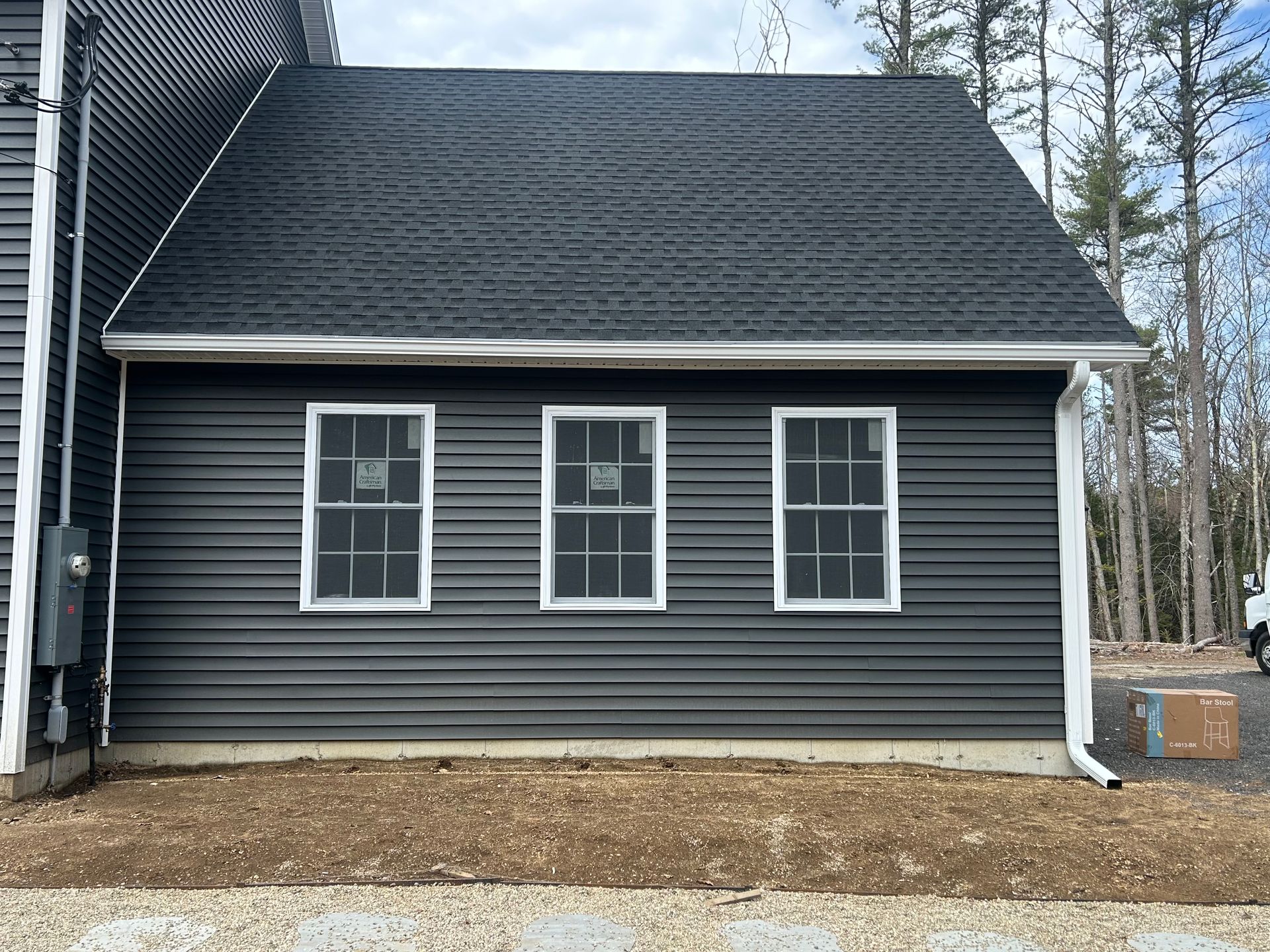Dark gray house exterior with three white-trimmed windows and a steep roof, viewed from the side.