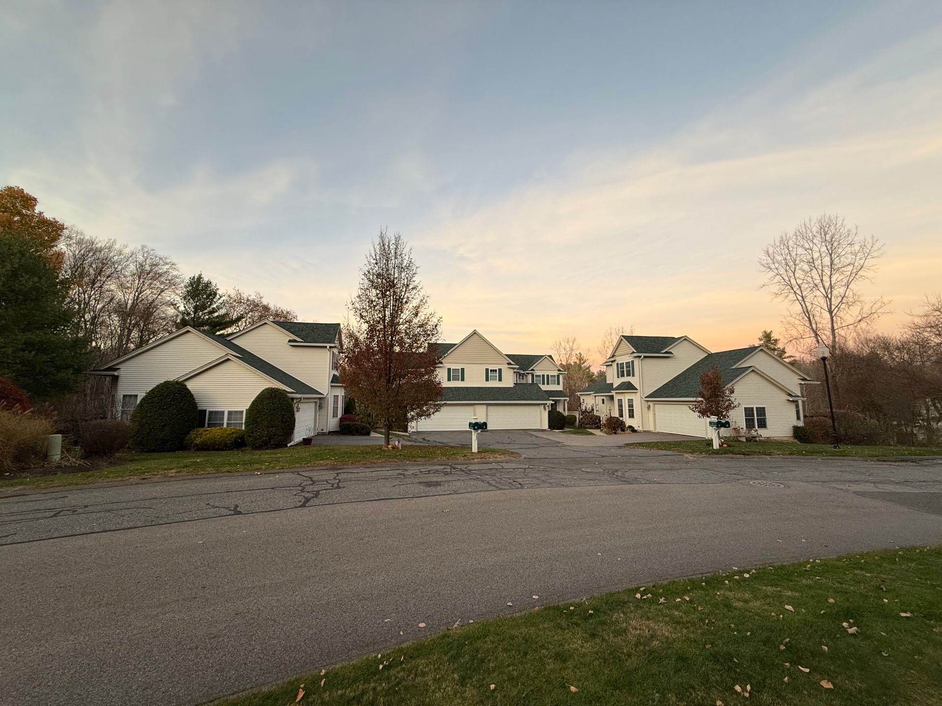 Quiet suburban street with white houses at sunset and a gravel driveway in the foreground